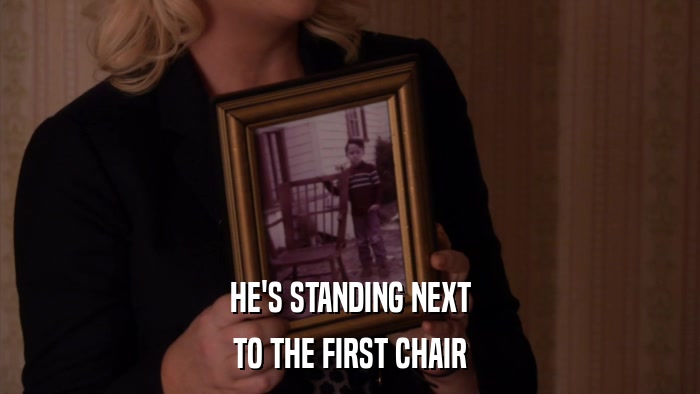 HE'S STANDING NEXT TO THE FIRST CHAIR 