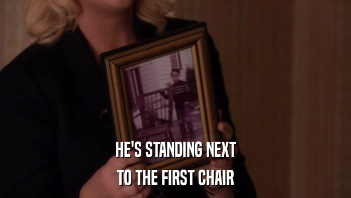 HE'S STANDING NEXT TO THE FIRST CHAIR 