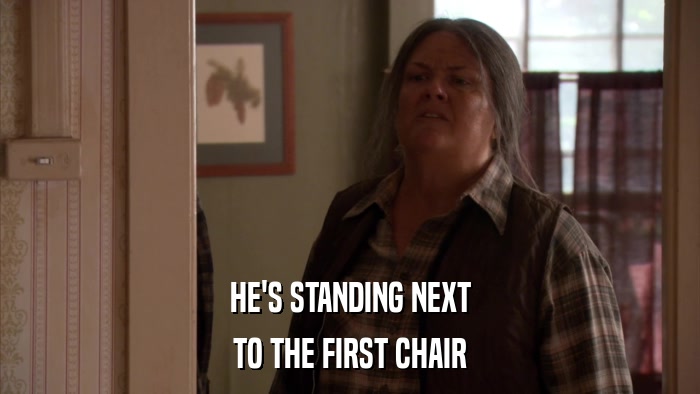 HE'S STANDING NEXT TO THE FIRST CHAIR 