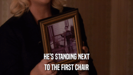 HE'S STANDING NEXT TO THE FIRST CHAIR 