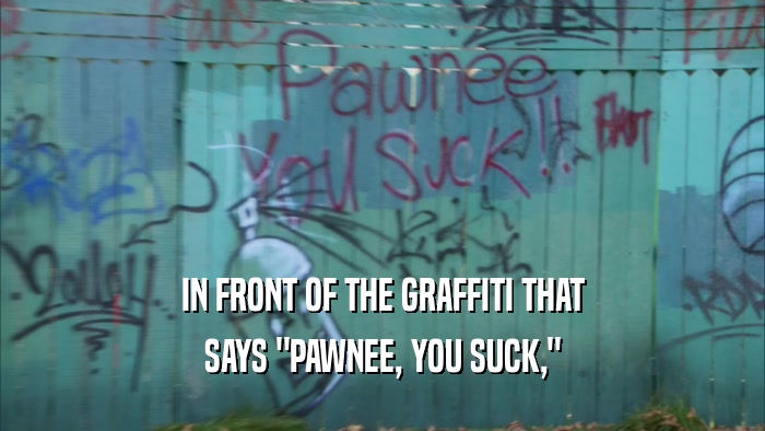IN FRONT OF THE GRAFFITI THAT SAYS 
