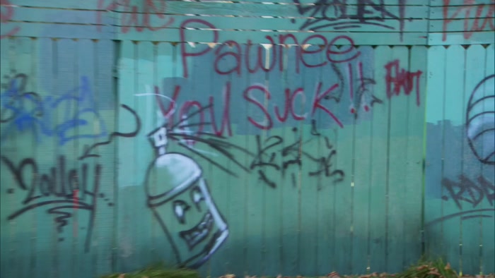IN FRONT OF THE GRAFFITI THAT SAYS 