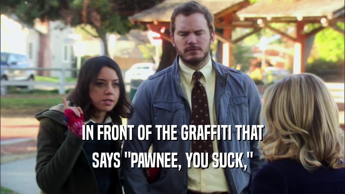IN FRONT OF THE GRAFFITI THAT SAYS 